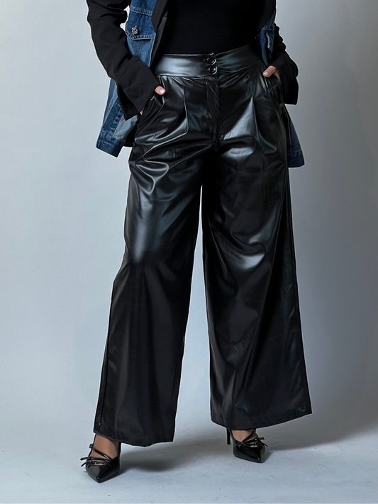 Woman wearing black leather pants, black top, and blue denim jacket against a gray background